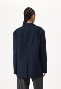 Marinblå blazer med en strukturert passform, notched lapeller og bakre sliss. Laget av glatt stoff, vist uten frontdetaljer.