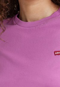 Fialové bavlněné tričko s kulatým výstřihem a krátkými rukávy; na levé straně má malé červené logo Levi's.