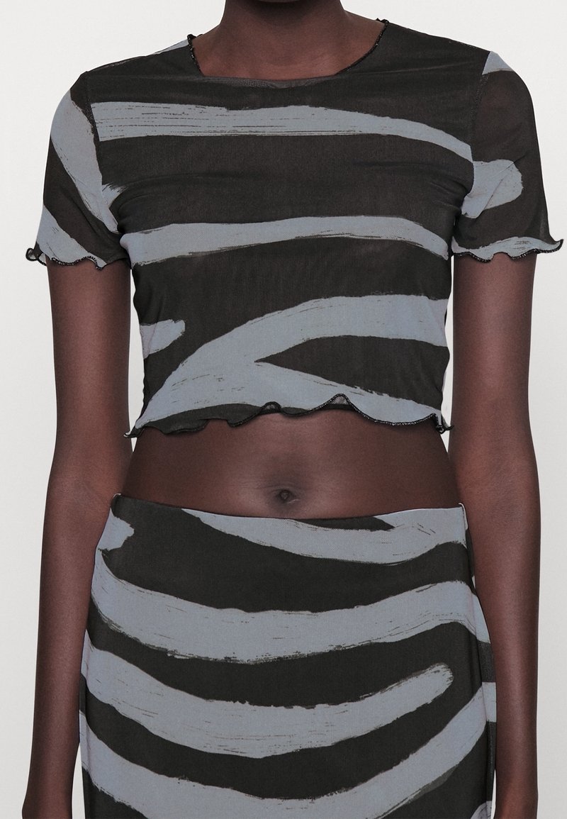 Kortärmad, croppad topp i genomskinlig svart tyg med blå abstrakta ränder. Har vågiga kanter och en rund halsringning.