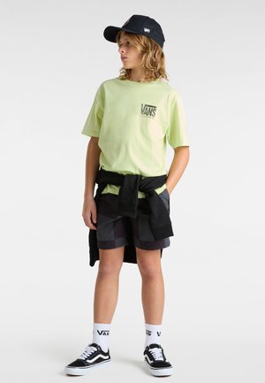 Camiseta de manga corta verde lima con el logo de Vans, pantalones cortos negros con un estampado de cuadros, sudadera negra atada a la cintura, gorra negra y zapatillas Vans.
