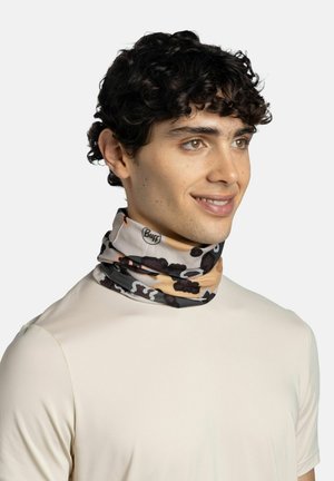 Junger Mann mit lockigem Haar, der ein beiges Hemd und ein mehrfarbiges Camouflage-Halstuch mit dem "Buff"-Logo trägt.