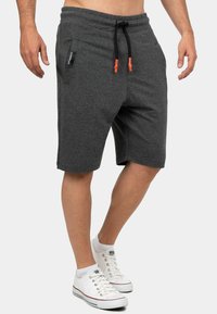 Grijze katoenen shorts in een katoenmix met een elastische tailleband, een zwart en oranje trekkoord, zijzakken en een relaxed fit, gedragen met witte sneakers.
