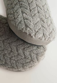 Grå slippers med en tekstureret, uldlignende overdel, der har et hævet bladmønster og en glat, grå sål.