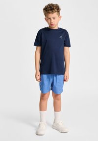 T-shirt bleu marine à manches courtes, assortie à un short bleu clair. Des baskets blanches et des chaussettes blanches à la cheville complètent la tenue.