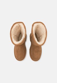 Botas ankle em camurça castanha, com um interior macio em pele de ovelha na cor creme e acabamentos cosidos, apresentando um bico redondo e sola plana em borracha.