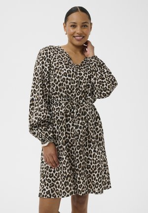 Donna sorridente, indossa un vestito a stampa leopardata fino al ginocchio con maniche lunghe a sbuffo e cintura in vita, su uno sfondo chiaro e uniforme.