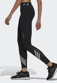 Mallas de alto rendimiento en negro con acentos de malla, que presentan rayas diagonales blancas en las piernas inferiores y una cinturilla con logotipo.