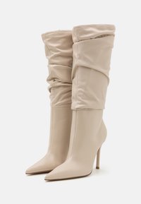 Bottes en cuir beiges jusqu'aux genoux avec un haut décontracté, un bout pointu et un talon aiguille haut. Texture lisse avec des détails minimaux.