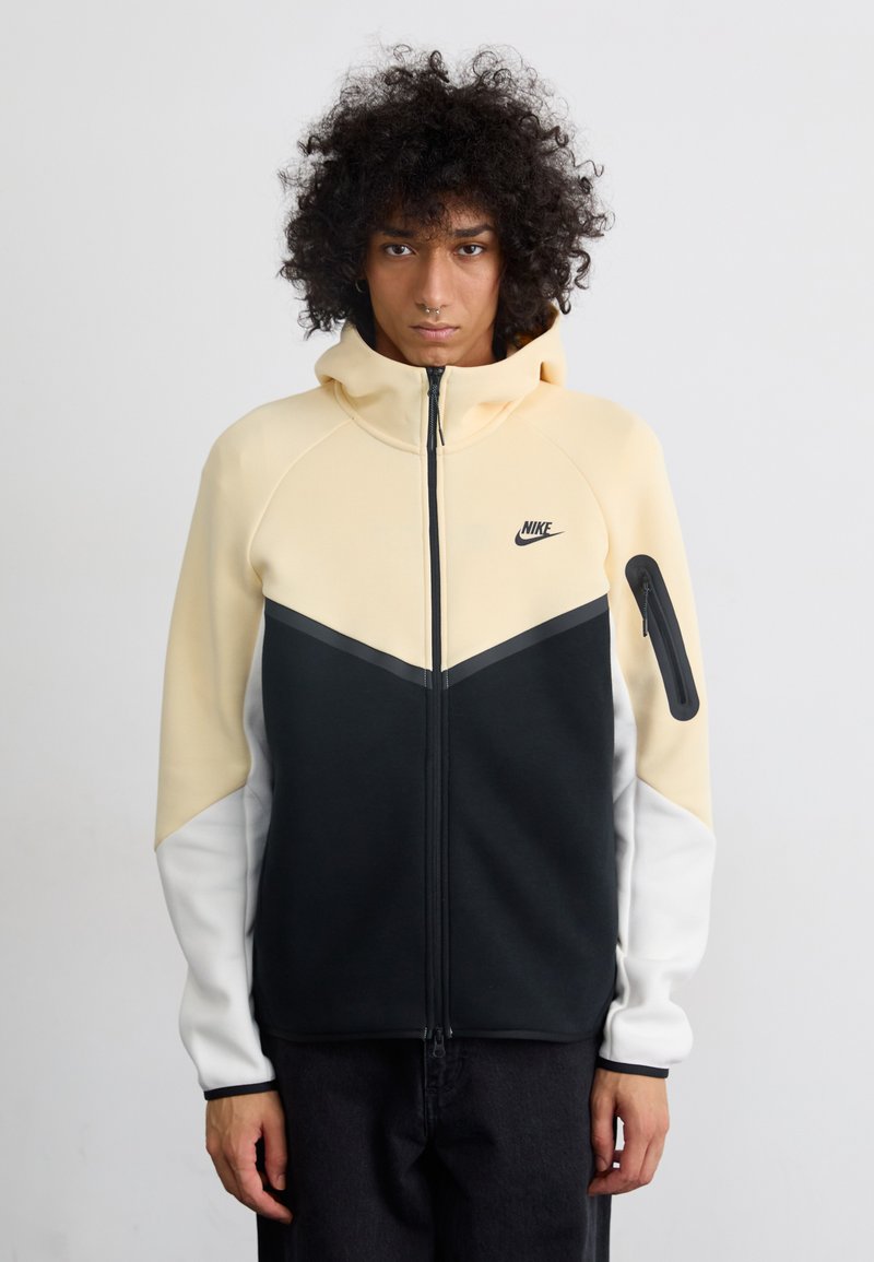 Nike kapucis džemperis ar rāvējslēdzēju ir izstrādāts ar krāsu bloka dizainu, kurā ir gaiši dzeltenas, melnas, baltas un pelēkas akcenti. Mīksts audums un rāvējslēdzēja kabata uz piedurknes.