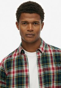 Camisa de cuadros con patrones en rojo, verde y amarillo, cuello abotonado y una camiseta blanca debajo.