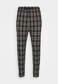 Svart och vit rutiga tapered byxor med elastisk midja och dragsko, visade mot en enkel vit bakgrund.