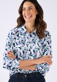 Geprinte blouse met een bladerenpatroon in tinten blauw en lavendel, voorzien van een knoopsluiting aan de voorkant en lange mouwen met knopen bij de manchetten.