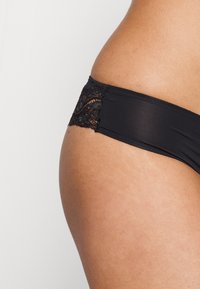 Shorty bikini noir en tissu lisse avec un accent en dentelle texturée à l'arrière. Le design est minimaliste avec une taille basse.