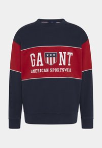 Felpa blu navy e rossa con scritta bianca "GAUNT American Sportswear" e logo a scudo con stelle e strisce sul petto.