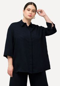 Camicia oversize blu navy con colletto e chiusura a bottoni; presenta maniche a tre quarti con fessure, realizzata in un tessuto morbido e leggero.