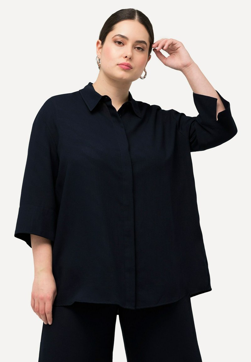 Camicia oversize blu navy con colletto e chiusura a bottoni; presenta maniche a tre quarti con fessure, realizzata in un tessuto morbido e leggero.
