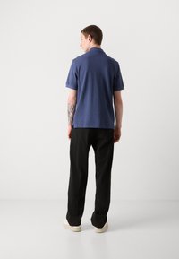 Marineblaues Polohemd mit strukturiertem Finish, kurzen Ärmeln und klassischem Kragen, kombiniert mit schwarzen Hosen und weißen Turnschuhen.