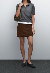 Maglione polo grigio a maglia, under t-shirt bianca, gonna in velluto a coste marrone, scarpe slip-on nere, con una borsa marrone. Texture lisce e design casual.