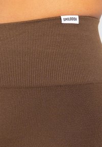 Leggings a coste marroni con un ampio cinturino vita e un'etichetta bianca con la scritta "SMILODOX". Il materiale appare liscio con una leggera lucentezza.