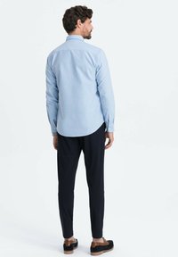 Lichtblauw overhemd met lange mouwen en een button-down kraag, gecombineerd met donkere broek en bruine schoenen, zichtbaar van de achterkant.