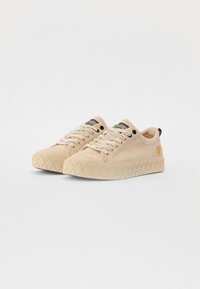 Beige casual sneakers featuring a suede upper, round toe, textured rubber sole with diamond pattern, and black logo accents on the tongue.