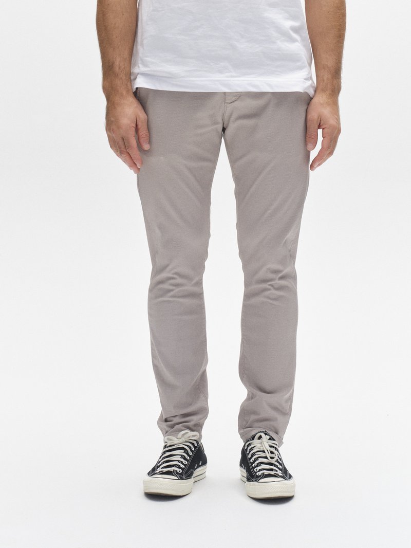 Pantalones de algodón gris claro con corte slim, frente plano y textura sutil, combinados con zapatillas negras y blancas con cordones.