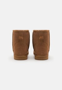 Brown suede ankle boots with a soft texture, featuring a stitched seam and back pull tab. The soles are flat and made of rubber.