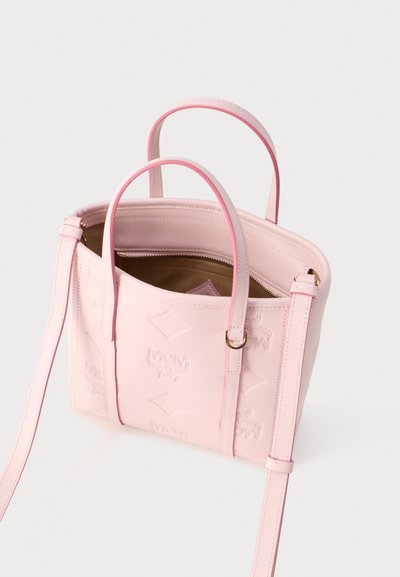 Τσάντα χειρός από ανοιχτό ροζ δέρμα με ανάγλυφα λογότυπα MCM, διπλές λαβές, ρυθμιζόμενο ιμάντα ώμου και ανοιχτό φερμουάρ που αποκαλύπτει καφέ εσωτερική επένδυση.