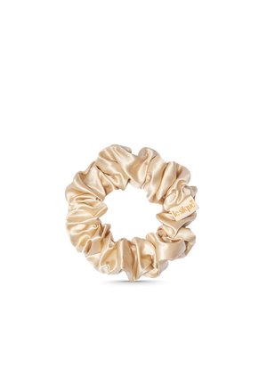 Chouchou en satin beige avec tissu froncé et petite étiquette attachée, isolé sur fond blanc.