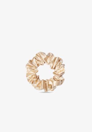 Chouchou en satin beige avec tissu froncé et petite étiquette attachée, isolé sur fond blanc.