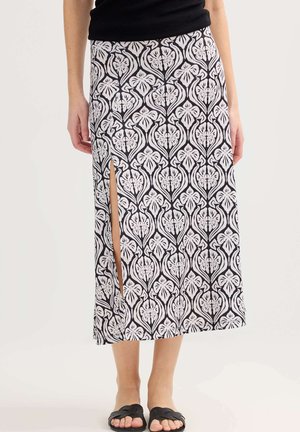 Falda midi con estampado floral en blanco y negro y abertura hasta el muslo, combinada con top negro y sandalias slip-on negras tejidas.