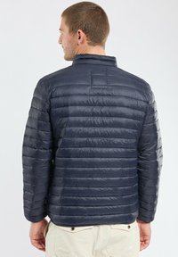 Veste matelassée bleu marine avec col montant, couture horizontale uniforme et un léger éclat, idéale pour un usage décontracté.