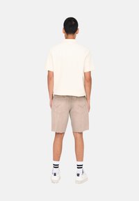 Camisa de manga corta color crema, pantalones cortos de mezclilla beige con bordes deshilachados, zapatillas blancas con detalles en púrpura y calcetines a rayas blanco y negro.