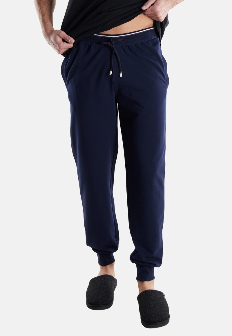 Navy cotton sweatpants with a drawstring waist, ribbed cuffs, and contrasted waistband detailing. Worn with gray slip-on slippers.