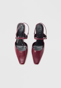 Bordeauxkleurige leren slingbacks met een vierkante neus, dunne enkelband, en zwarte binnenzolen met gegraveerde merknaam. Soepele textuur.