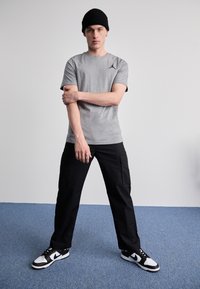 Tricou gri cu mânecă scurtă, cu un logo Air Jordan alb, asortat cu pantaloni cargo negri și adidași alb-negru. Se poartă o căciulă neagră.
