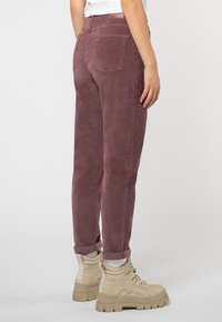 Samt Hosen in Bordeaux, mit geradem Schnitt, zwei Gesäßtaschen und umgekrempelten Säumen, kombiniert mit beigen High-Top-Sneakern.