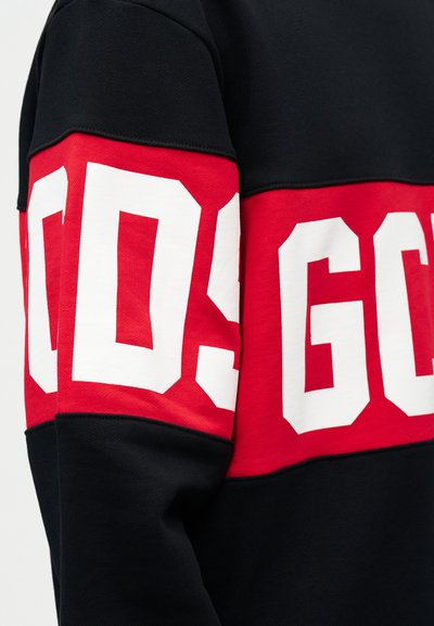 Juoda ir raudona ilgomis rankovėmis džemperis su didelėmis baltomis blokinėmis raidėmis „GCDS“ per visą krūtinę ir rankoves.