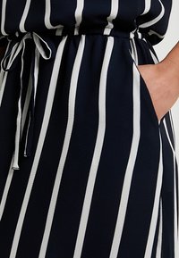 Navy sininen kangas valkoisilla pystysuorilla raidoilla, jossa on joustava vyötärö, naru- ja sivutaskut. Sujuva pinta.