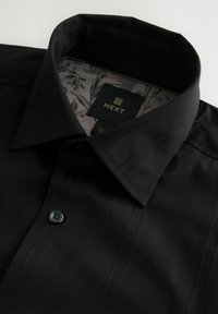 Schwarze Hemdjacke mit gemustertem Innenkragen, strukturiertem Stoff mit vertikalen Streifen und einem Etikett mit der Marke "NEXT".