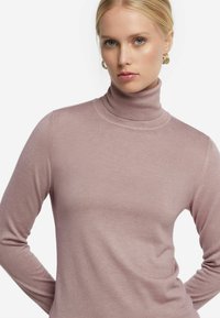 Ljusrosa polotröja i slät tyg, med långa ärmar och en figurnära silhuett med subtila sömmar.