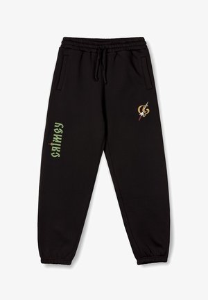 Pantalones de chándal negros en tejido suave, con cintura elástica, bolsillos laterales y logos en verde y dorado en la pierna izquierda.