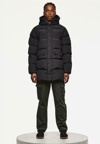 Schwarze Pufferjacke mit Kapuze, mit einem gesteppten Design, Fronttaschen und einer leicht lockeren Passform, kombiniert mit olivgrünen Cargo-Hosen und schwarzen Schuhen.