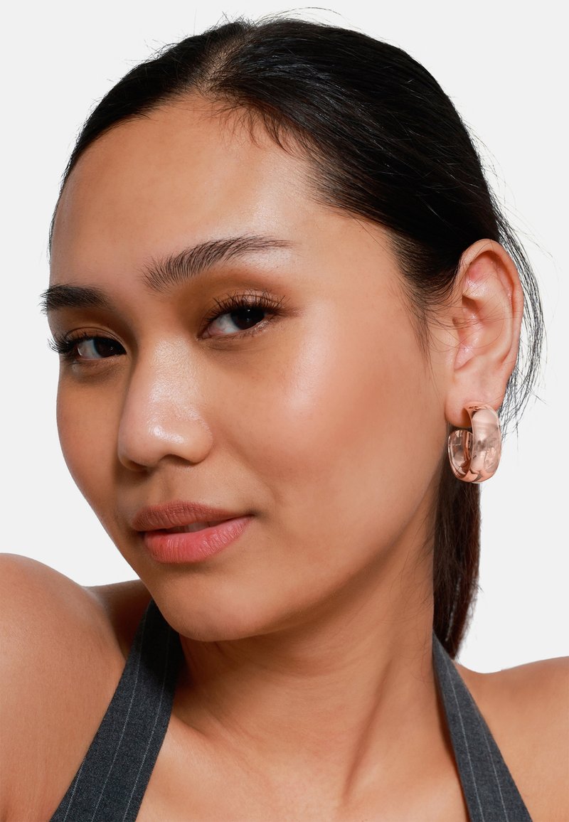 Translucente rosa Creolen aus Acryl. Runde Form mit glatter Textur und glänzender Oberfläche, getragen von einem Model mit dunklem Haar.