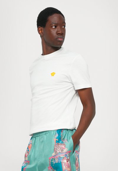 Vit bomull t-shirt med slim fit, med en liten gul broderad design på bröstet. Korta ärmar, rund halsringning.