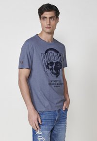 Pilka medvilninė marškinėlė su priekyje esančia kaukolės grafika, užrašu "RUGGED" ir žaibų motyvais. Trumpomis rankovėmis, su mažu logotipu kairiajame rankovėje.