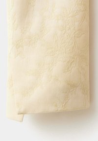 Tissu couleur crème avec une broderie florale subtile représentant des feuilles et des vignes en relief.