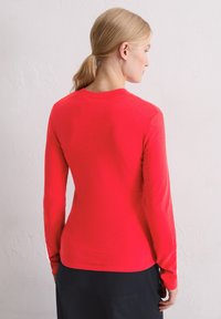 Czerwona bawełniana koszulka z długim rękawem, z zaokrąglonym dekoltem i dopasowanym krojem, o gładkiej fakturze bez widocznych wzorów.