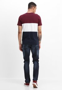Herre t-skjorte med kort erme som har et fargeblokkdesign i burgunder, hvitt og marineblått. Kombinert med mørkeblå jeans og røde sneakers.