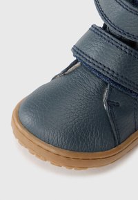 Donkerblauwe leren schoen met een gestructureerd oppervlak, met een ronde neus, klittenbandsluitingen en een rubberen buitenzool in een tan kleur.